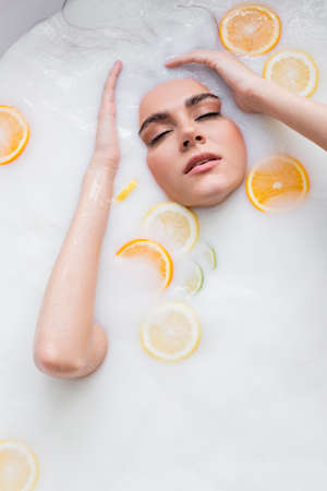 pretty woman with closed eyes bathing in milk with sliced citrusesの写真素材