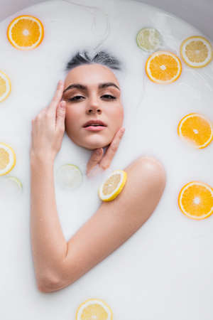 sensual woman looking at camera while bathing in milk with citrus slicesの写真素材