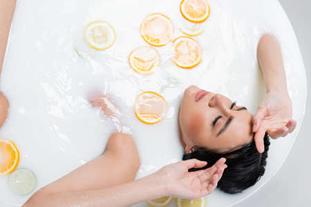 overhead view of woman with closed eyes in milky bath with fresh citrusesの写真素材