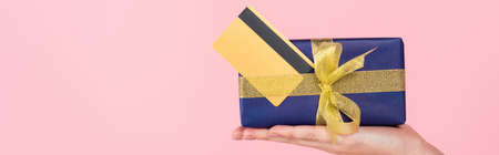 partial view of woman showing gift box and credit card isolated on pink, bannerの写真素材