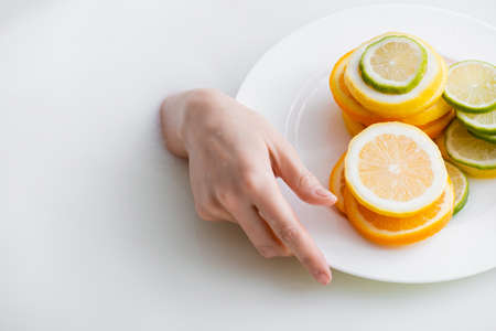 partial view of female hand in milk bath near plate with sliced lemon, lime and orangeの写真素材