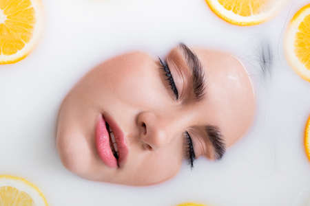 close up view of female face with closed eyes in milk bath with citrus fruitsの写真素材