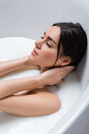 pretty, young woman touching neck while taking milk bathの写真素材