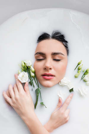 top view of young woman in milk bath with fresh eustoma flowersの写真素材