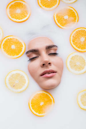 top view of female face in milk bath with sliced lemon and orangeの写真素材