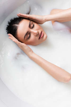 overhead view of sensual woman touching hair while bathing in milk