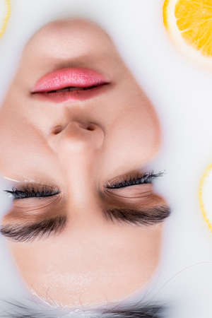 close up view of female face in bath with milk and sliced orangeの写真素材