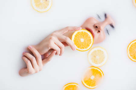 top view of woman holding orange slice in milk bathの写真素材