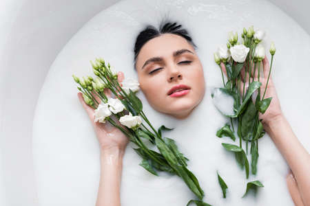 young woman with closed eyes enjoying bathing in milk with eustoma flowersの写真素材
