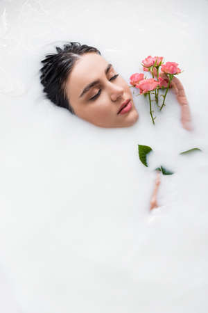young woman relaxing in milk bath with pink roses