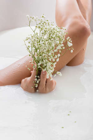 partial view of woman holding white, tiny flowers while enjoying milk bathの写真素材