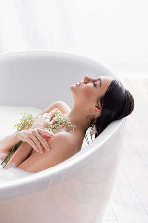 woman with closed eyes taking milk bath with gypsophila flowersの写真素材