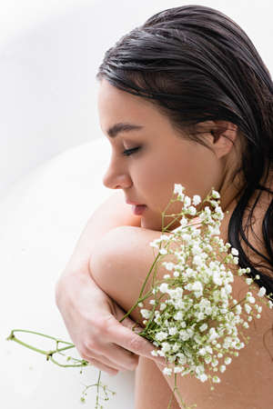 woman with closed eyes taking milk bath while holding gypsophila flowersの写真素材