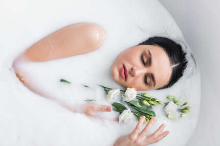 pretty woman relaxing in milk bath with eustoma flowersの写真素材