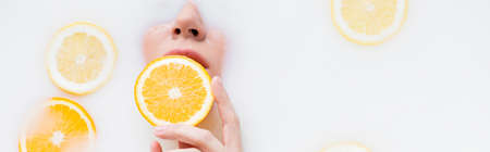 top view of woman holding orange slice in milk bath, bannerの写真素材
