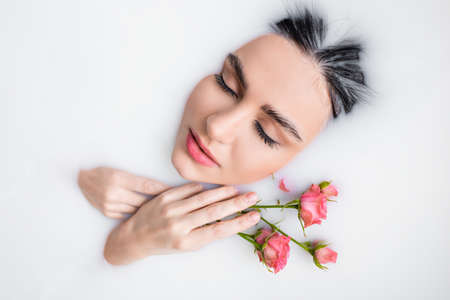 young woman with closed eyes and pink roses bathing in milkの写真素材