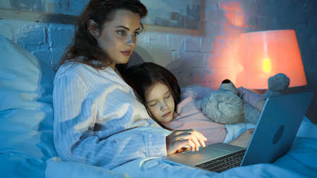Woman using laptop near sleeping kid on bed