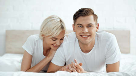 joyful man and cheerful woman holding hands on bed