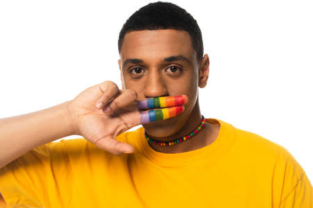 african american man covering mouth with fingers painted in lgbt colors isolated on whiteの写真素材