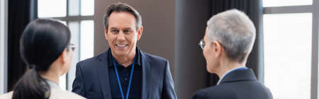 Smiling businessman looking at blurred colleagues, banner