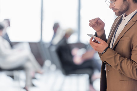Cropped view of businessman using smartphone near blurred conference roomの写真素材