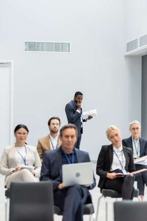 African american businessman holding documents near blurred interracial business people in conference roomの写真素材