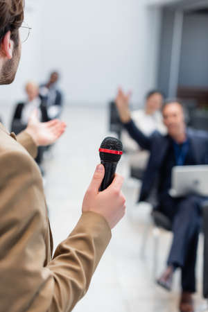 young lecturer with microphone pointing at blurred audience during seminarの写真素材