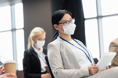 asian businesswoman in medical mask holding digital tablet during seminarの写真素材