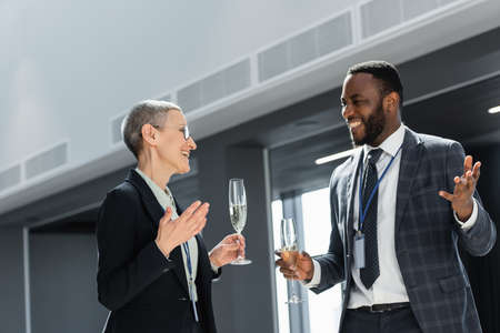 cheerful multicultural business people holding champagne during discussion on conferenceの写真素材