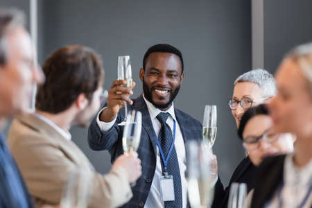selective focus of african american businessman holding champagne glass near interracial colleagues