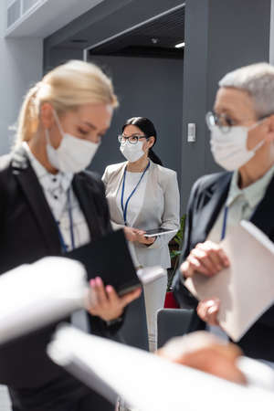 selective focus of asian businesswoman in medical mask near colleagues talking on blurred foreground