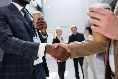 interracial businessmen shaking hands near colleagues on blurred backgroundの写真素材
