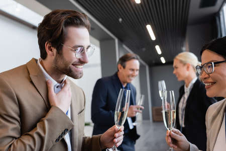 young businessman holding champagne during conversation with asian colleague