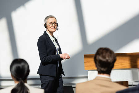 mature lecturer in headset looking at participants on blurred foregroundの写真素材