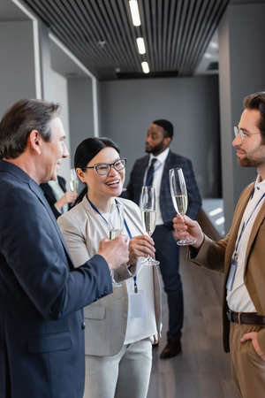 cheerful interracial businesspeople holding champagne glasses during break in symposiumの写真素材
