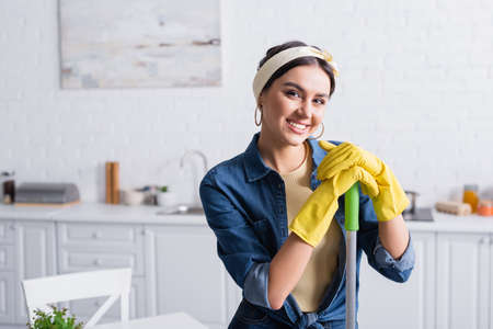 Housewife in rubber gloves holding mop and smiling at cameraの写真素材