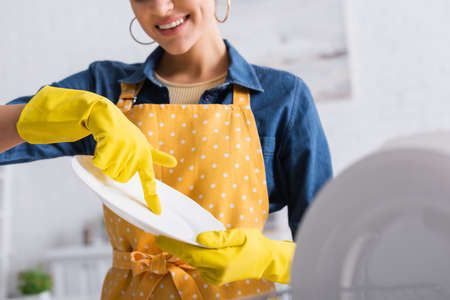 Cropped view of smiling woman in rubber gloves holding clean plateの写真素材