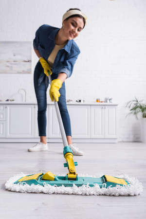 Mop on floor in hands of smiling woman on blurred background in kitchen