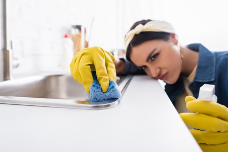 Sponge in hand of housewife on blurred background washing kitchen sink