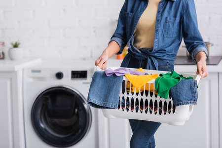 Cropped view of housewife holding basket with clothes at home