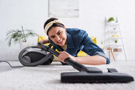 Angry woman cleaning carpet with blurred vacuum cleaner in living roomの写真素材