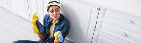 Dissatisfied housewife with detergent and sponge in kitchen, banner