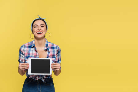 Cheerful housewife holding digital tablet isolated on yellow