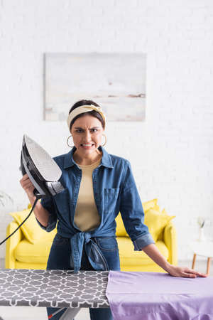 Aggressive housewife holding iron near clothes on boardの写真素材
