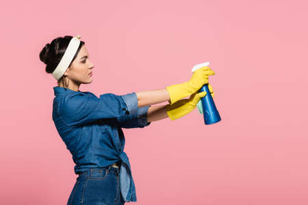 Side view of housewife holding detergent and rag isolated on pink
