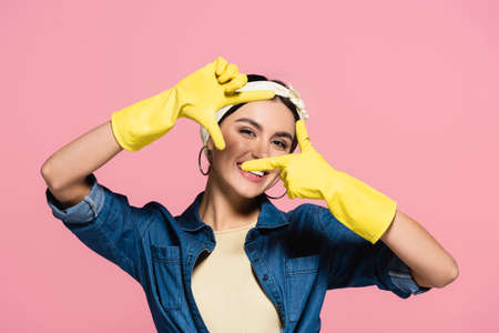 Cheerful woman in rubber gloves looking at camera isolated on pinkの写真素材