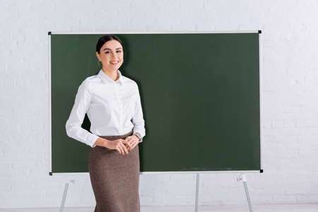 Positive teacher in formal wear standing near chalkboard with copy spaceの写真素材