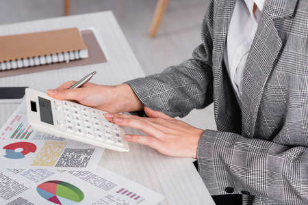 Cropped view of businesswoman using calculator near documents on table