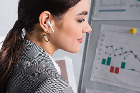 Side view of businesswoman in earphone standing near blurred flipchart