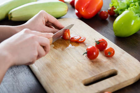 cropped view of woman cutting cherry tomatoes on chopping board near vegetablesの写真素材
